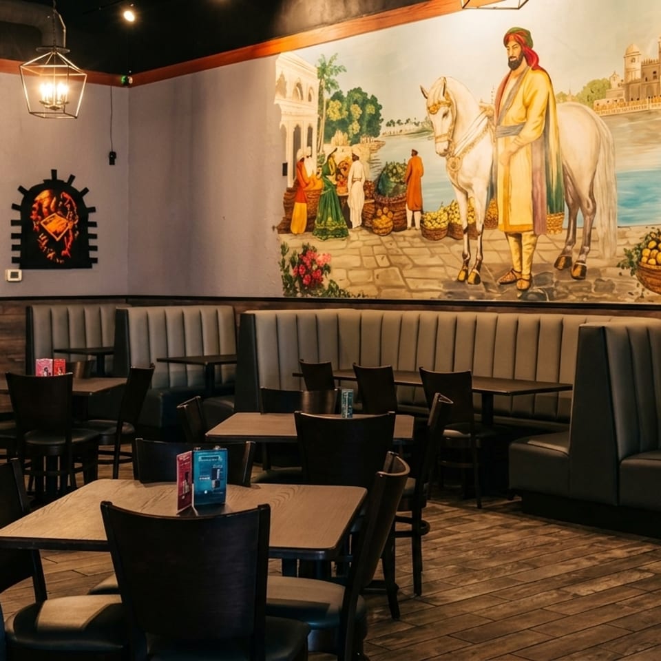Restaurant interior with booths, tables, chairs, and a large mural depicting an Indian market scene.